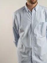 Camisa de corte regular confeccionada en tejido Oxford de algodón, con diseño de rayas verticales finas. Presenta cuello abotonado, cierre frontal con botones y un bolsillo en el pecho.