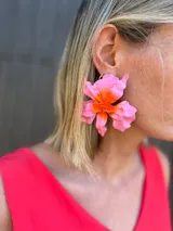 Aretes grandes con forma de flor, con pétalos en tonos de rosa claro y centro en naranja vibrante. Tienen un acabado brillante.