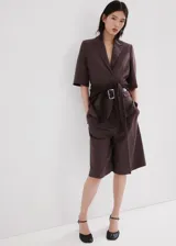 Blazer de lino y viscosa color marrón, de diseño recto, cuello en pico con solapa, mangas tres cuartos, dos bolsillos con solapa, cierre frontal con botones y cinturón integrado a juego.