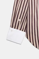Camisa de manga larga con estampado de rayas verticales en tonos marrón y beige. Presenta cuello solapa y puños anchos en color blanco a contraste, con cierre frontal de botones.