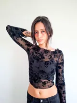 Remera de manga larga confeccionada en microtul transparente con diseño de flores aterciopeladas en color negro, cuello bote y costuras frontales visibles.