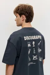 Remera de corte oversize color blanco tiza, de manga corta y cuello redondo, con pequeño estampado gráfico azul en el pecho.