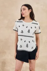 Remera de algodón color blanco con bordados florales y geométricos en color negro. Presenta cuello redondo, mangas cortas y un diseño con franjas horizontales bordadas.