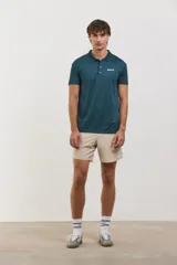 Chomba deportiva de manga corta, color verde oscuro, con cuello polo y cierre frontal de dos botones. Presenta un diseño entallado con tejido técnico transpirable y elástico, ideal para actividades deportivas.