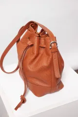 Cartera tipo botellero color marrón con efecto trenzado, tamaño mediano, cierre con frunce, correa ajustable con hebilla para usar al hombro o cruzada, doble bolsillo interior (uno con cierre).