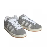 Championes Adidas modelo Campus 00s, confeccionados en gamuza gris con las icónicas tres tiras laterales en blanco. Presentan cordones blancos, suela de goma color crema con base de caucho natural y diseño de corte bajo.