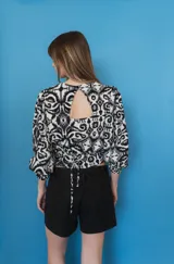 Blusa estampada en blanco y negro, con cuello redondo y mangas globo de puños elastizados largos. Presenta tiras ajustables en los laterales.
