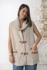 Chaleco de lana merino color beige, con cuello alto acanalado y cierre frontal con broches de cuerno y presillas de cuero. Incluye dos bolsillos delanteros con detalles de cuero.