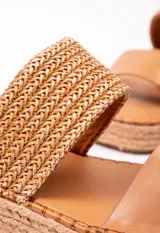 Sandalia con doble tira en el empeine, una de cuero color tostado y otra tejida en rafia. Plataforma de yute de 3.5 cm de alto.