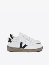 Zapatillas Veja modelo V-12, color blanco con logo lateral en negro y suela color caramelo.