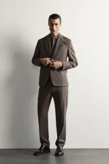 Blazer regular fit de Zara, confeccionada en tejido de lino y lana con diseño a cuadros en tonos marrones y grises. Cuenta con solapas de muesca, cierre frontal de un botón y bolsillos con solapa en la cadera.
