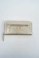 Billetera rectangular de cuero sintético con acabado metalizado dorado, cierre perimetral y bolsillo frontal con cierre y detalle de tachas.