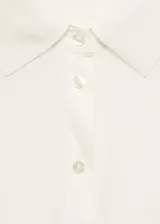 Camisa color crema de tejido fluido, manga corta, cuello camisero y cierre frontal con botones.
