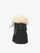 Bota de cuero negro con plataforma robusta y taco medio. Presenta detalles de piel de oveja en el borde superior y la lengüeta, con sistema de ajuste mediante cordones negros.