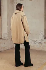 Campera de corderito color beige con detalles en cuero sintético negro, cierre frontal con botones a presión y bolsillos con cierre.
