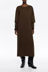 Vestido largo de corte holgado en color marrón, con cuello redondo y mangas largas de tul superpuestas. Presenta un diseño minimalista con sutiles detalles brillantes en el tejido principal.