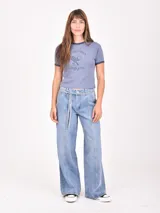 Remera ajustada color azul grisáceo, con cuello redondo y ribete en contraste en el cuello y las mangas. Presenta un estampado frontal con texto que dice "Beverly Hills Tennis Club Est. 1985" y un gráfico de una raqueta de tenis y una copa de vino cruzadas.