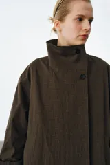 Trench oversize de Zara Woman Collection, confeccionado en mezcla de algodón con estampado de cuadros pequeños. Presenta cuello alto, cierre frontal con botones, mangas largas con trabillas ajustables y bolsillos laterales.