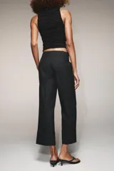 Pantalón marrón de tiro alto con bolsillos delanteros y traseros. El bajo está acabado con vuelta. Cierre frontal con cremallera y ganchos metálicos.