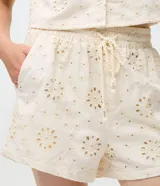 Short femenino de tiro alto color crudo, confeccionado en sarga con textura floral calada de broderie. Cuenta con cintura elástica y cordón ajustable para anudar.