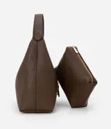 Bolso de hombro tipo hobo mediano, color marrón oscuro, con textura de cuero granulado. Presenta un cierre frontal decorativo de herradura metálica dorada sobre una solapa. Incluye una correa de hombro ancha y un neceser interior.