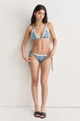 Bikini de dos piezas con estampado azul y verde, con bordes de encaje blanco de crochet. El corpiño es triangular y regulable, y la bombacha es regulable con lazos laterales.