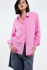 Camisa oversize de popelina a rayas celestes y blancas, con cuello camisero, manga larga con puños abotonados, cierre frontal con botones y un bolsillo en el pecho con etiqueta bordada.
