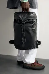 Mochila de piel negra de la colección especial Aaron Levine x Zara, con compartimento principal con solapa y hebilla, bolsillos exteriores en los laterales y asas ajustables.