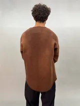 Buzo de lana merino afieltrada color negro con estampado abstracto plateado en el frente. Tiene cuello redondo y puños con forma que cubre levemente la mano. Es más largo en la parte inferior trasera.