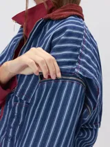 Campera de denim a rayas verticales con cuello de pana en color bordó. Presenta cierre frontal, mangas desmontables con cierre en los hombros, canesú en el pecho y bolsillos de parche cuadrados.