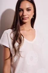 Remera de algodón color blanco con cuello en V y mangas cortas. Presenta un diseño con flores bordadas en relieve y detalles calados en el tejido.