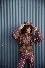 Campera impermeable con capucha y cierre frontal, con estampado de hojas en tonos marrones y ocres. Tiene bolsillos laterales ocultos y cordón ajustable en la cintura.