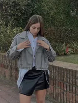 Mini falda negra de cuero sintético con corte irregular y detalle de hebilla metálica.