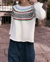 Sweater tejido a mano con hilo de algodón color crudo, con cuello redondo y mangas 3/4 con volados. Presenta un diseño geométrico en el pecho con detalles en negro, verde, rojo y azul.