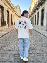 Remera blanca de algodón con corte oversize y estampado en la espalda de una playa con palmeras y una silla de playa.