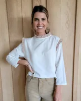 Blusa blanca de manga larga con cuello alto y volados en cuello y hombros.