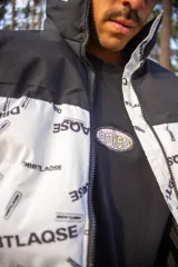 Campera puffer con diseño bicolor, presentando una parte superior en negro y el resto en blanco con estampado tipográfico de la marca. Posee cuello alto, cierre frontal completo y puños elásticos.