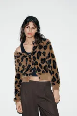 Chaqueta de punto con textura suave, cuello redondo y manga larga. Presenta un diseño de estampado animal print en tonos marrones y negros, con cierre frontal de botones.