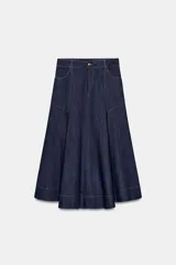 Falda midi de denim en color azul oscuro, con diseño evasé, bolsillos delanteros, costuras pespuntadas en contraste y cierre frontal con cremallera y botón metálico.