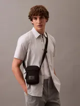 Cartera bandolera Calvin Klein color negro, confeccionada en nylon reciclado. Presenta correa ajustable, cierre superior con cremallera, bolsillo frontal y logo CK en relieve.