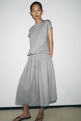 Vestido midi de Zara Woman Collection confeccionado en hilatura con lino, color gris. Presenta cuello redondo, manga corta caída, detalle de frunces y lazadas laterales en el mismo tejido, y cierre en la espalda.