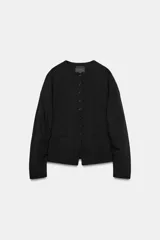 Chaqueta de cuello redondo y manga larga con pliegues, de color negro, con falsos bolsillos de vivo en el delantero y cierre frontal con botones.