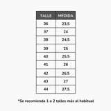 Zapatillas deportivas de mujer, estilo retro running, en tonos blanco y gris claro. Presentan una combinación de malla transpirable y paneles de gamuza sintética. La suela es gruesa y blanca, con una suela exterior de goma color caramelo. Detalle en el talón en color marrón.