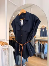 Camisa azul marino de manga corta con silueta relajada, cuello solapa y botones frontales en contraste. Cuenta con bolsillos con solapa en el pecho y viene con un cinturón trenzado de cuero sintético marrón.