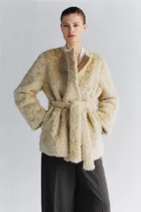 Abrigo de Zara Woman Collection con textura efecto pelo, cuello redondo y manga larga. Presenta un diseño cruzado con cinturón ajustable del mismo tejido y bolsillos delanteros.