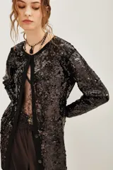Tapado negro de corte recto completamente cubierto de lentejuelas, con mangas largas y cierre frontal. Presenta un diseño elegante y brillante ideal para eventos nocturnos.