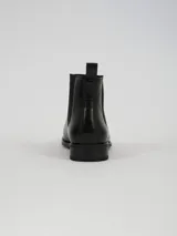 Botin tipo Chelsea de cuero sintético negro, con paneles laterales elásticos, tirador trasero y suela de goma dentada.