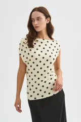 Top de poliéster negro con estampado de lunares blancos, diseño al cuerpo y cuello asimétrico de manga corta.