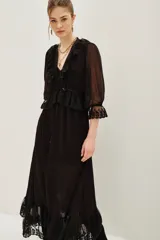 Vestido midi negro de estilo romántico, confeccionado en tejido semitransparente con detalles de encaje en el cuello, la cintura y el ruedo. Presenta mangas tres cuartos con terminación en encaje, escote en V con volados y un lazo de ajuste en la cintura.