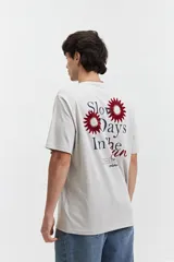 Remera de manga corta color gris claro, con cuello redondo y estampado pequeño en el pecho con texto en rojo y negro.